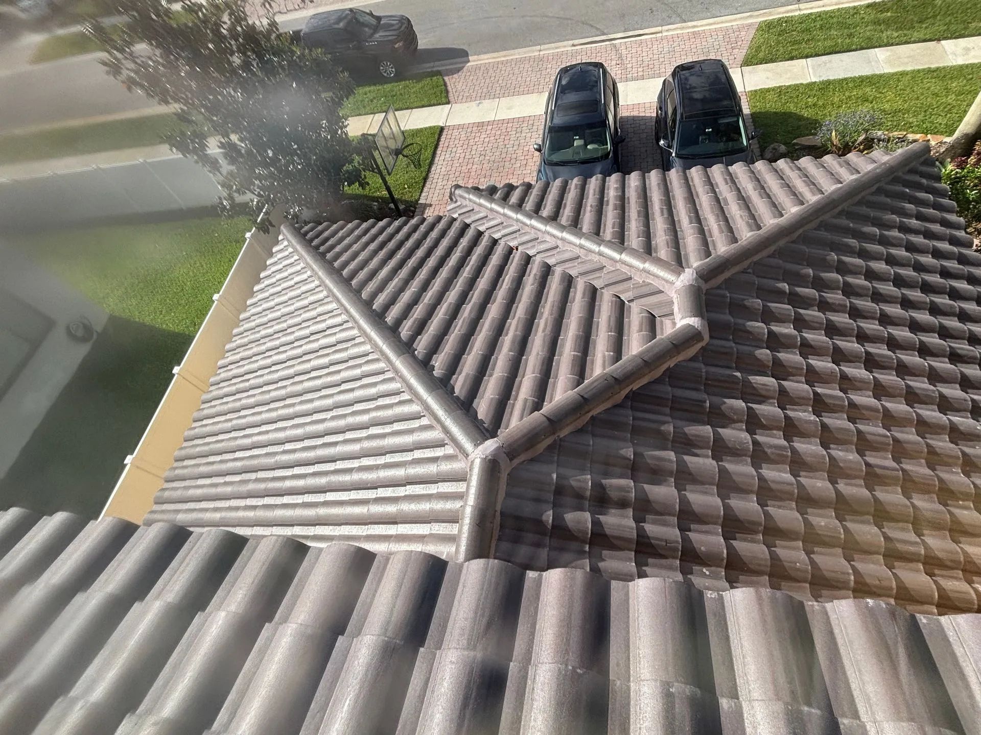Overhead view of a gray tiled roof with a water channel. Two cars parked on a brick driveway.