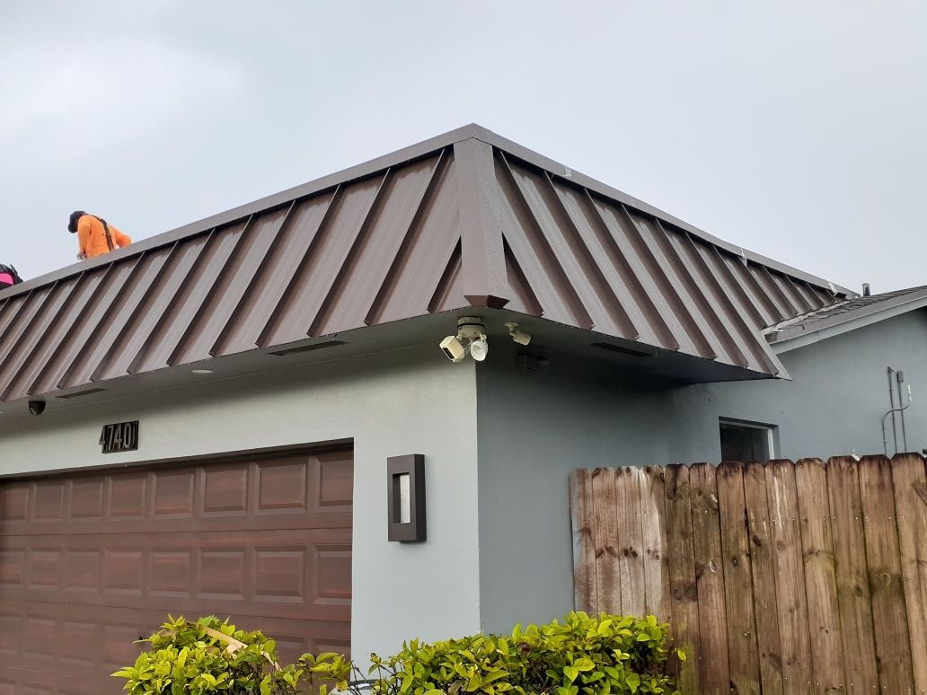 Brown metal roof on a light blue house with two security cameras and a brown garage door.