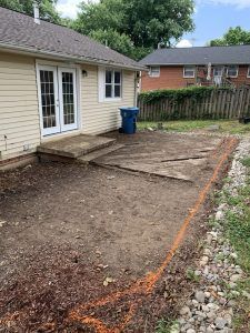 A backyard construction site showing a house with light siding, a concrete step, and an area marked with orange spray paint.