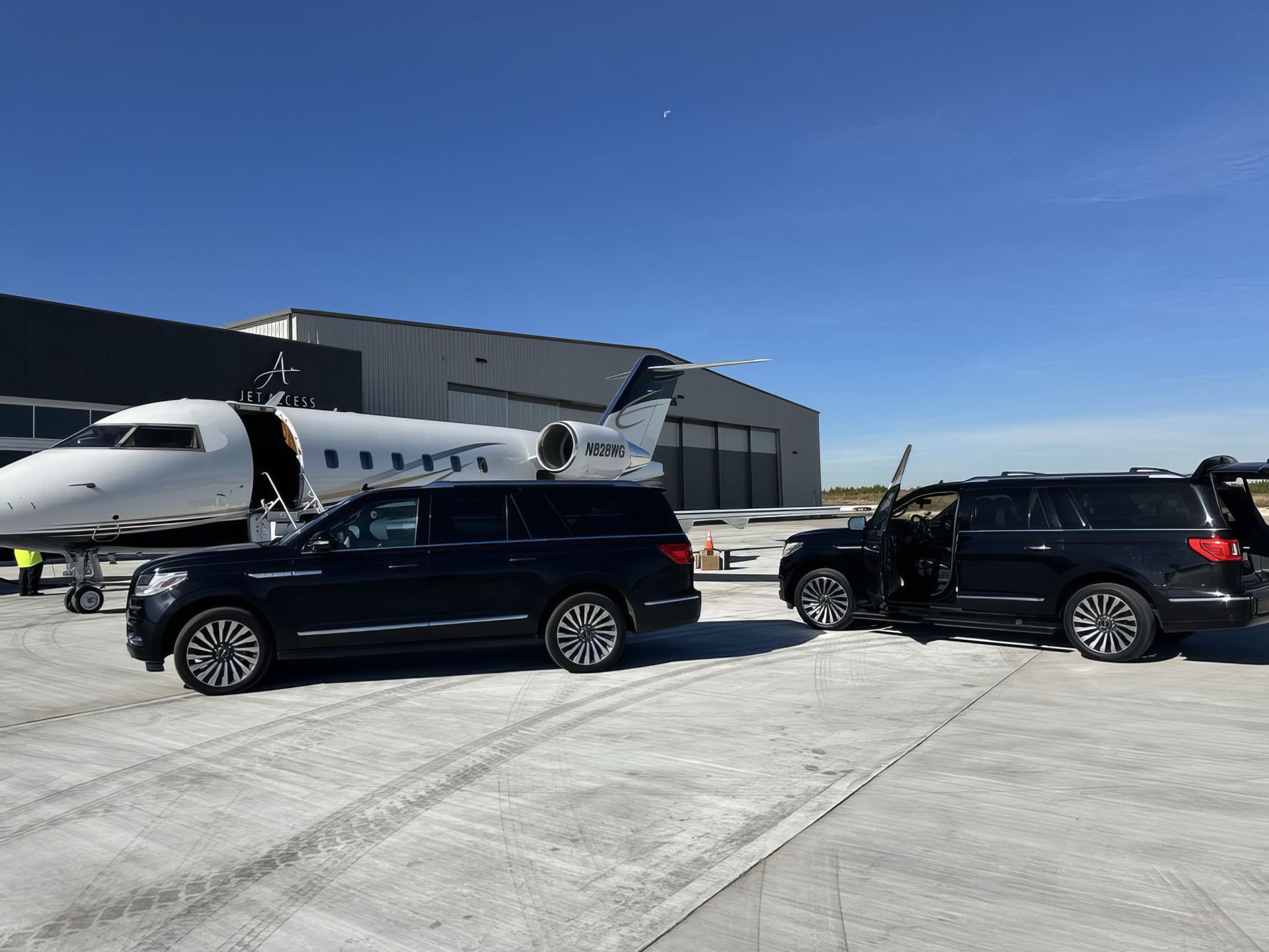 Private jet on snowy tarmac with two black SUVs parked in front of a hangar