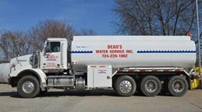 A white water service tanker truck parked on pavement with company branding and phone number visible