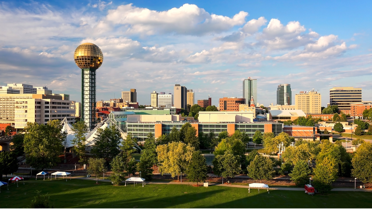 City skyline with a gold sphere tower, modern buildings, and trees under a partly cloudy sky.