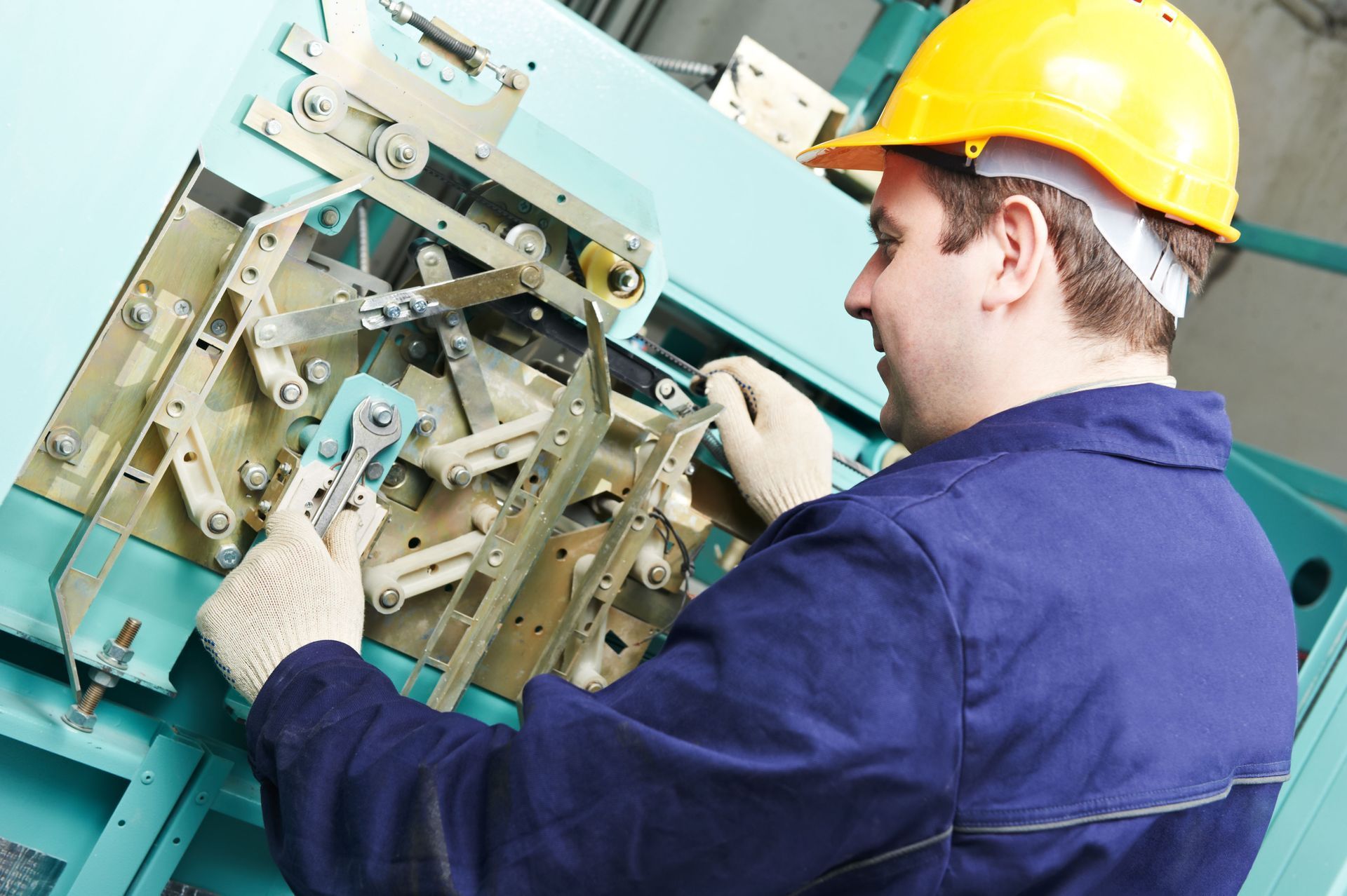 Technician in a yellow hard hat inspecting machinery with tools in an industrial setting