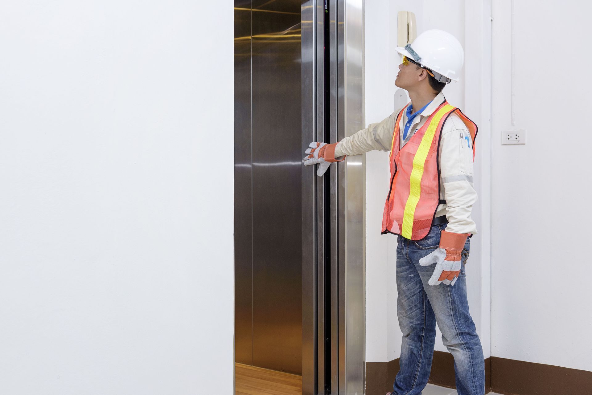 Worker in hard hat and safety vest opening an elevator door in a hallway.