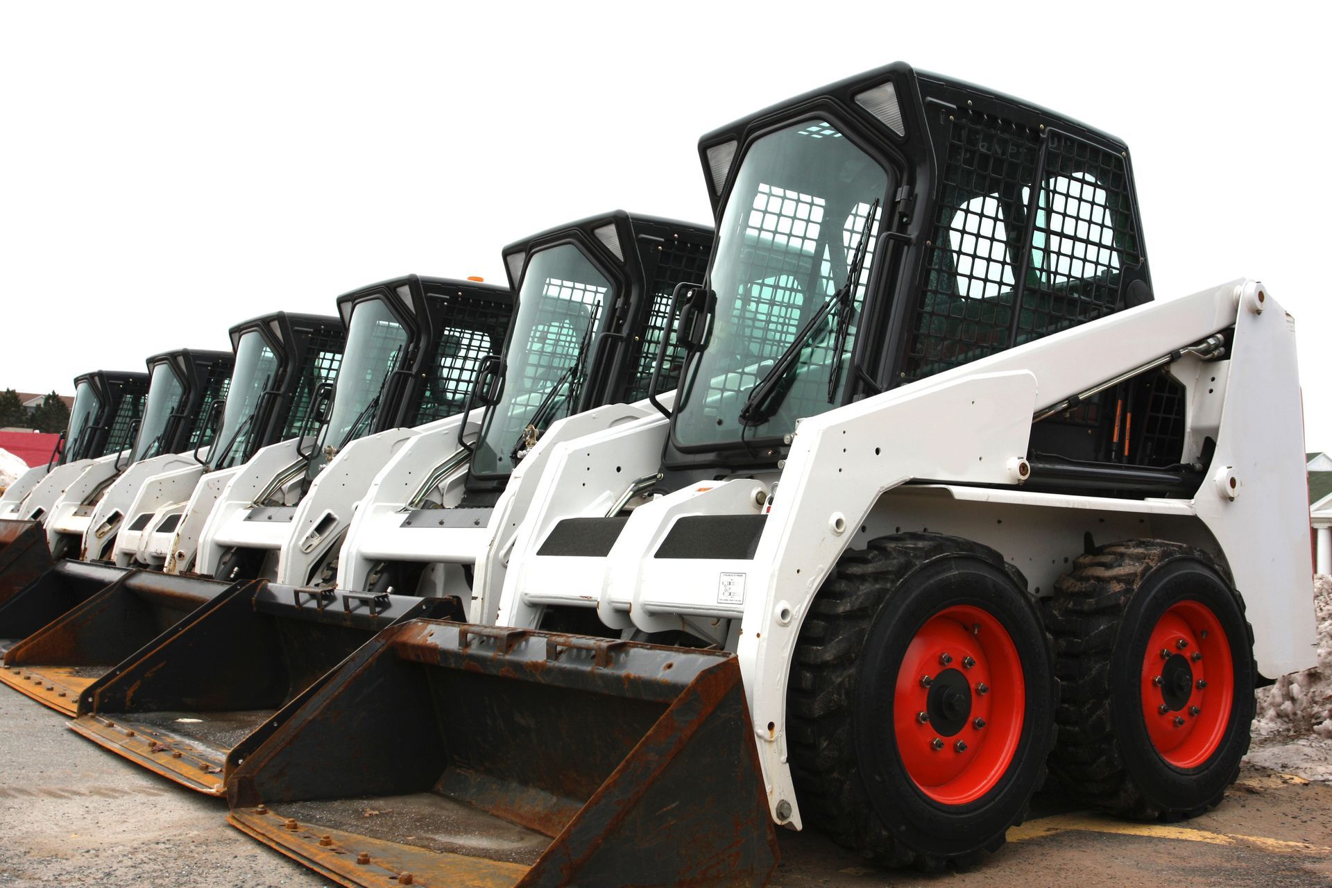 A row of skid steer loaders are lined up in a parking lot