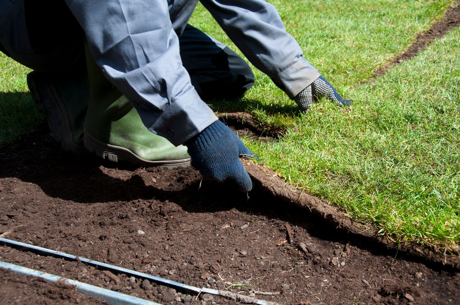 A person is kneeling down in the dirt next to a lawn.