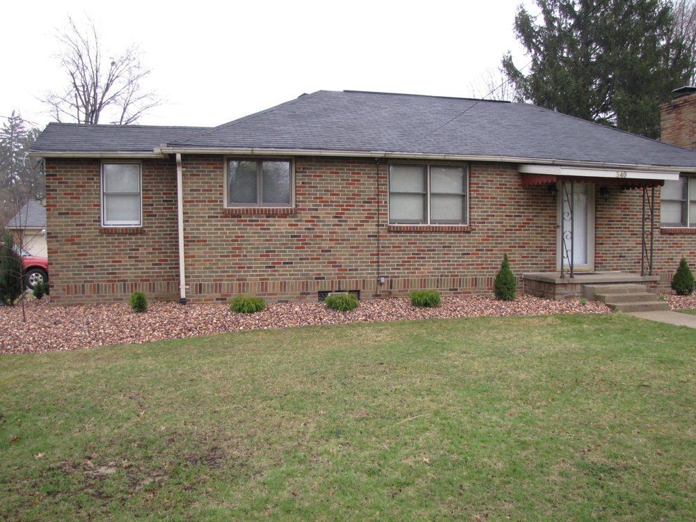 A brick house with a black roof and a lush green yard