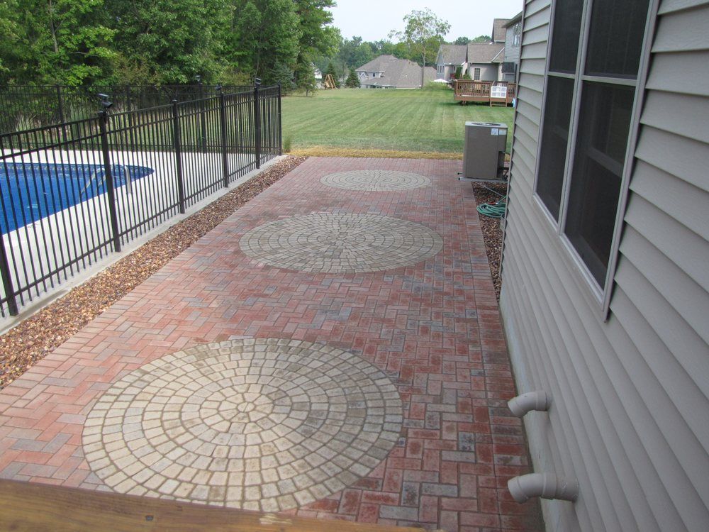 A brick walkway leading to a house with a pool in the background