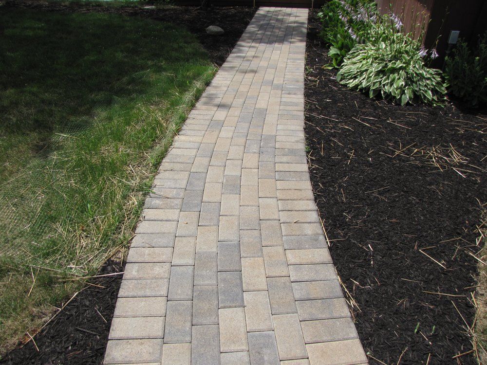 A brick walkway going through a lush green yard