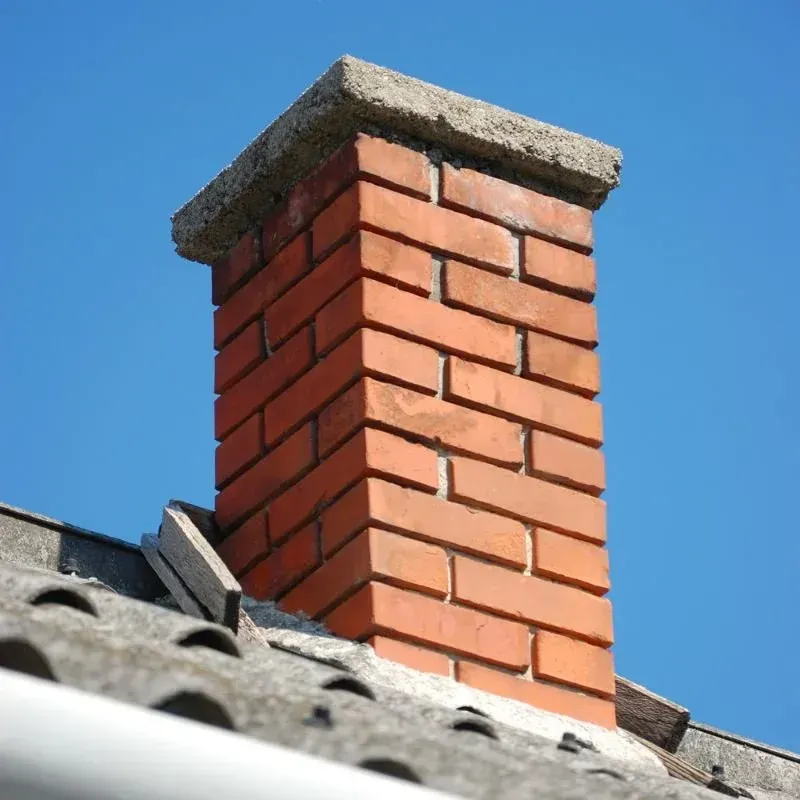 A brick chimney on top of a roof with a blue sky in the background