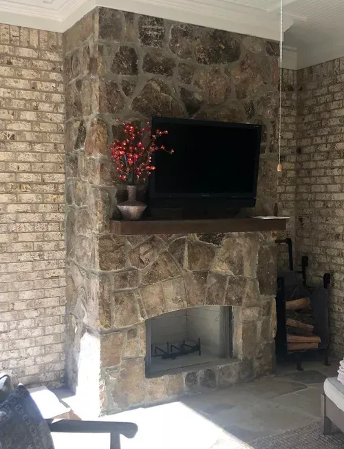 A living room with a stone fireplace and a flat screen tv.