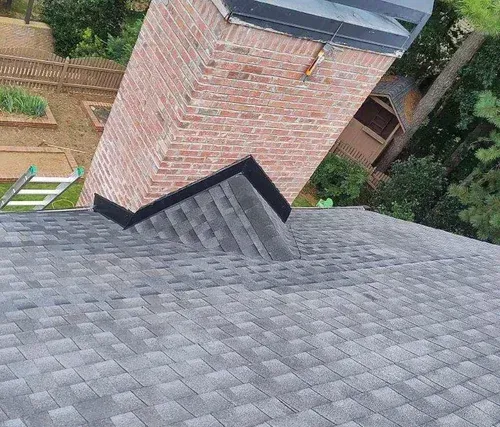 A brick chimney is sitting on top of a roof next to a ladder.