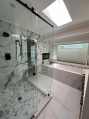Modern bathroom with marble tile, glass shower, black fixtures, and a skylight.