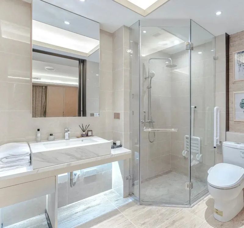 Modern, light-toned bathroom featuring a sleek marble vanity, large mirror, glass-enclosed shower, and white toilet.