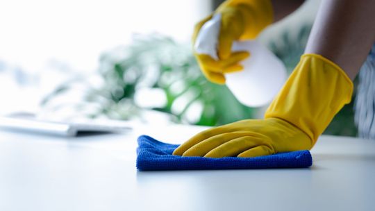 Yellow-gloved hands wiping a white surface with a blue cloth Yellow-gloved hands wiping a white surface with a blue cloth