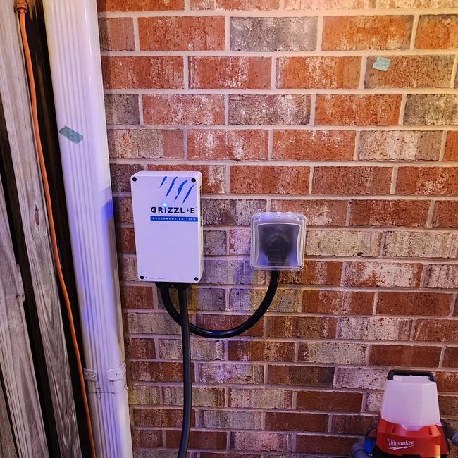 Outdoor brick wall with a small white electrical box and covered outlet, plus a cone at bottom right.