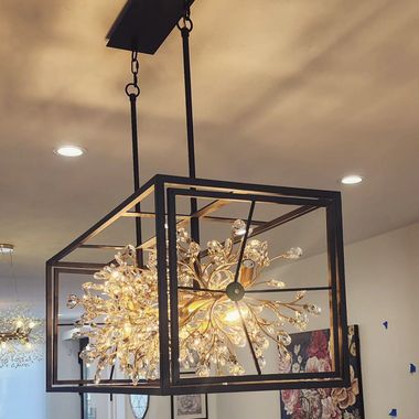 Black geometric pendant light with a starburst crystal chandelier inside, hanging in a modern room.