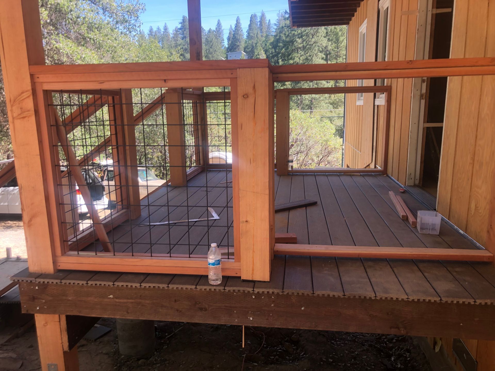 Unfinished wooden deck with a partially installed wire mesh railing and a water bottle on the decking.