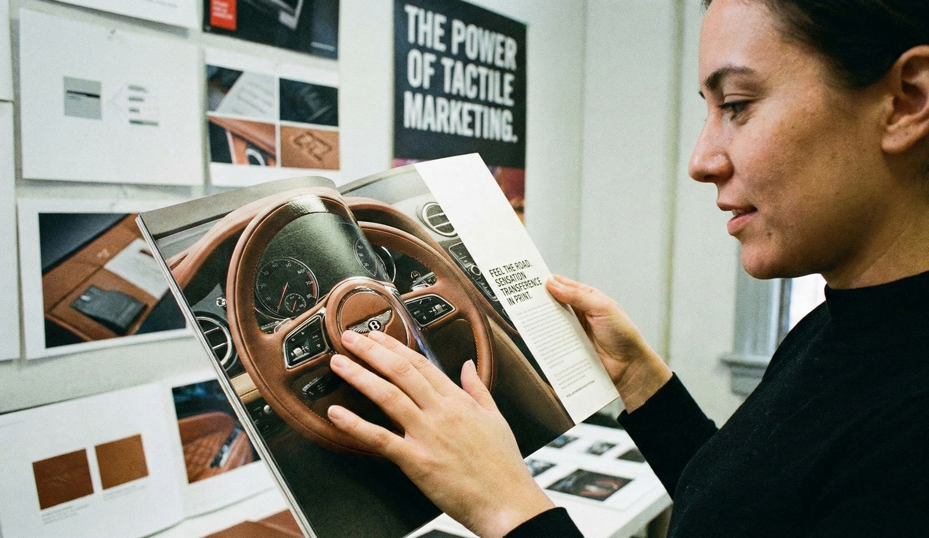 Woman examining a magazine with a car interior on display, in a room with design materials.