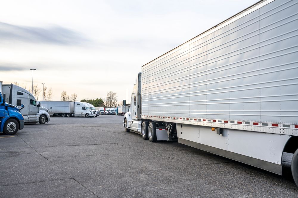 Parking lot with several white semi-trucks and trailers lined up under a cloudy sky