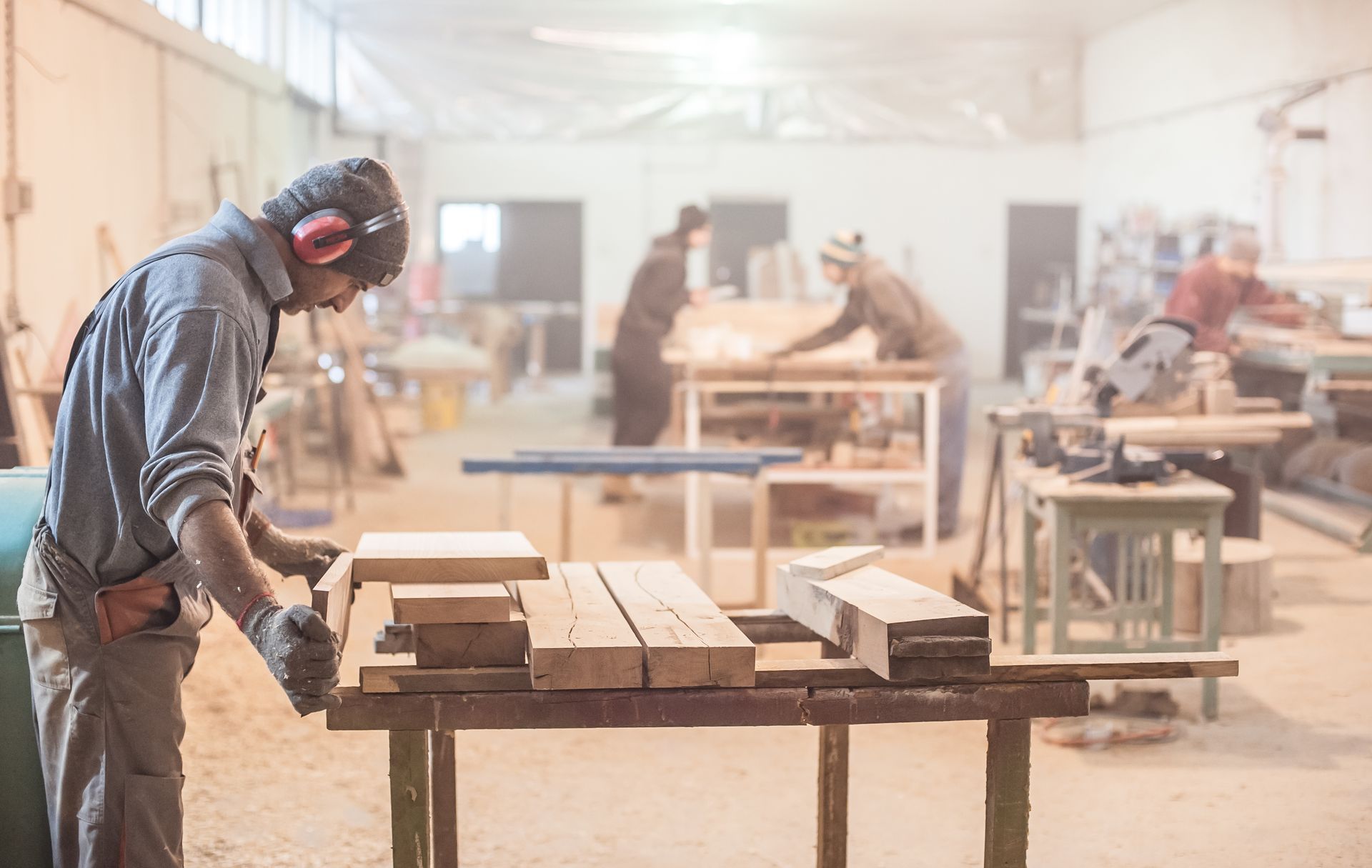 A man is working on a wooden table in a woodworking shop.