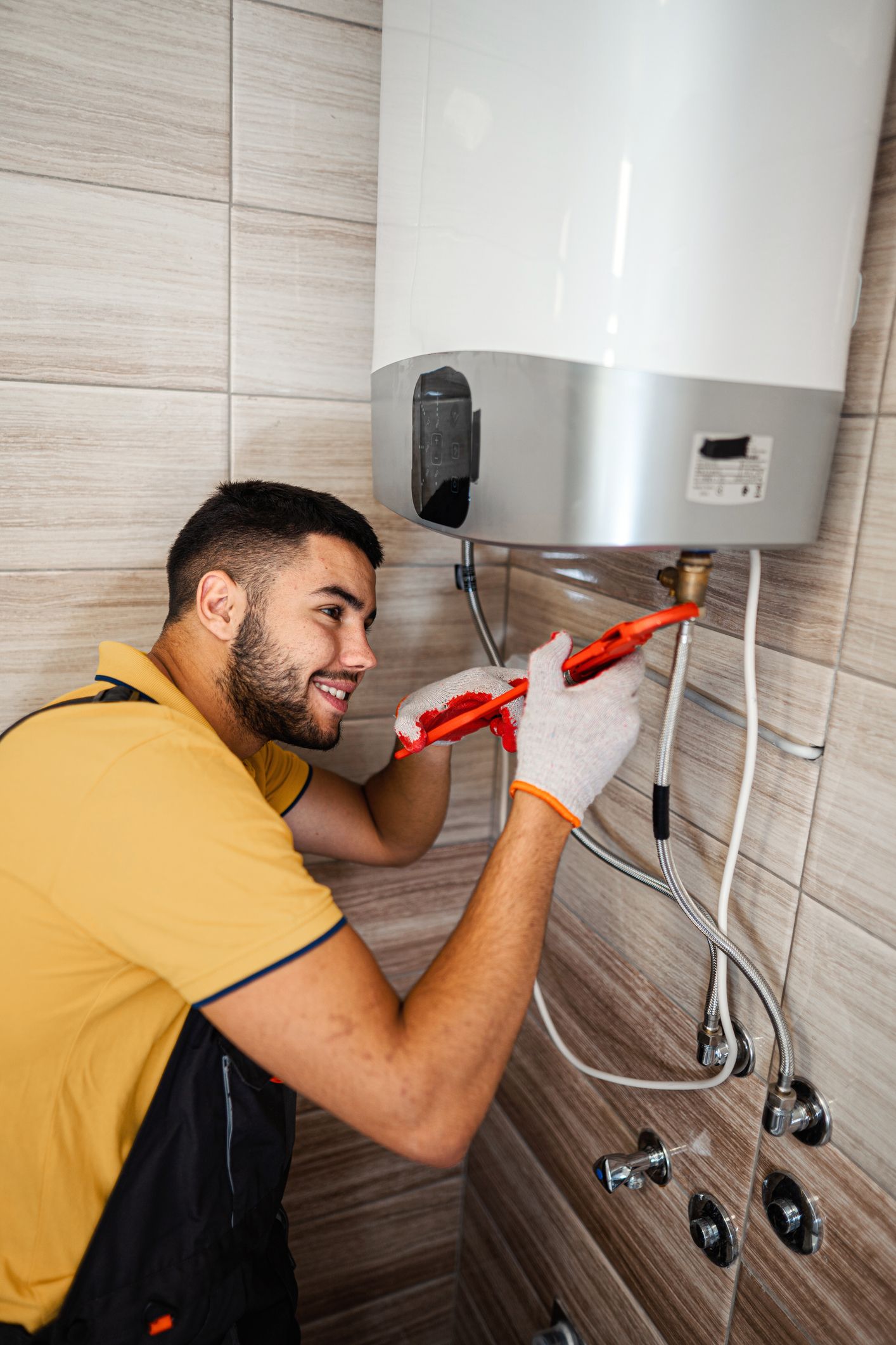 Plumber wearing gloves, working on a water heater in a bathroom.