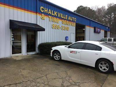 A white car is parked in front of chalkville auto & tire service.