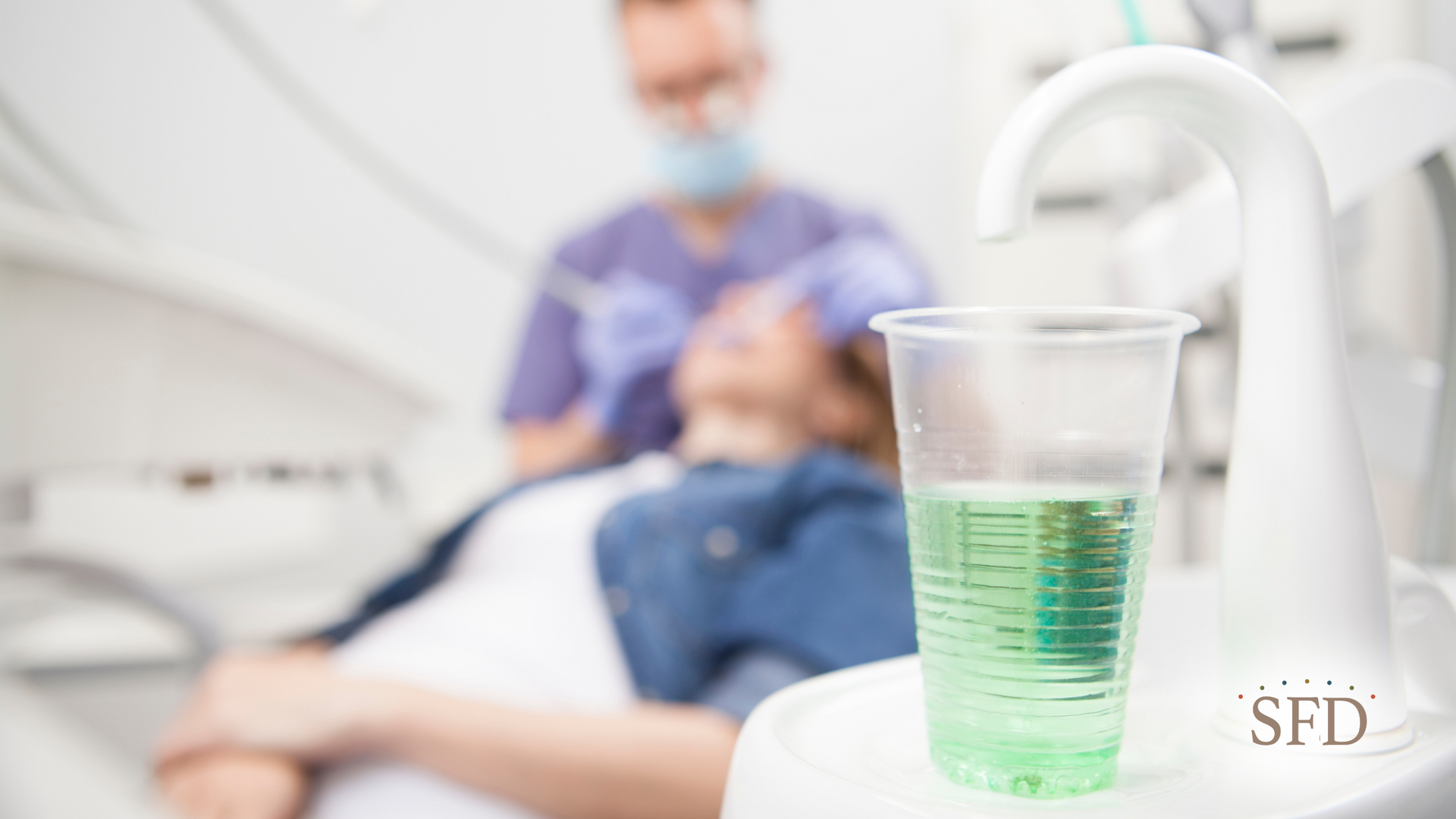 A person is sitting in a dental chair with a cup of mouthwash in front of them.