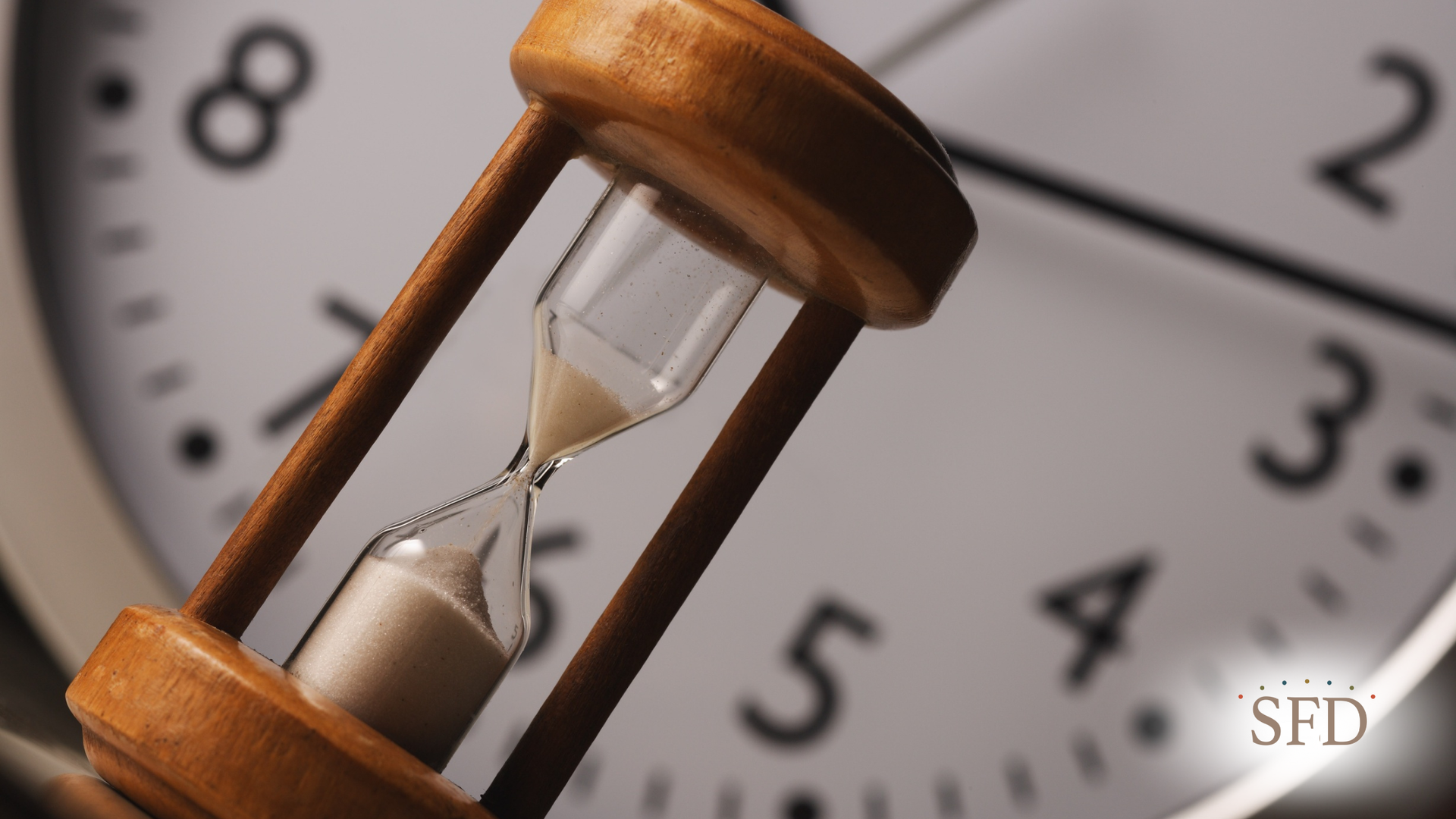 Hourglass and clock face. Sand flows through the hourglass with the clock face visible in the background.