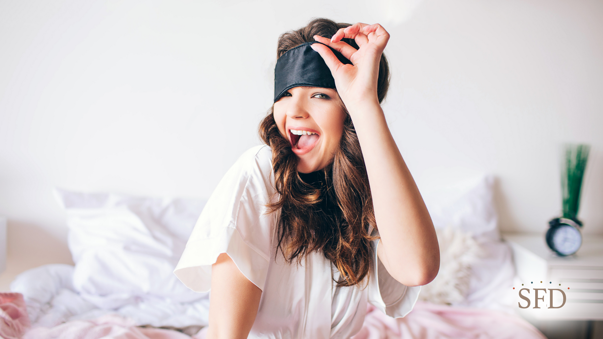 A woman wearing a sleep mask is sitting on a bed.