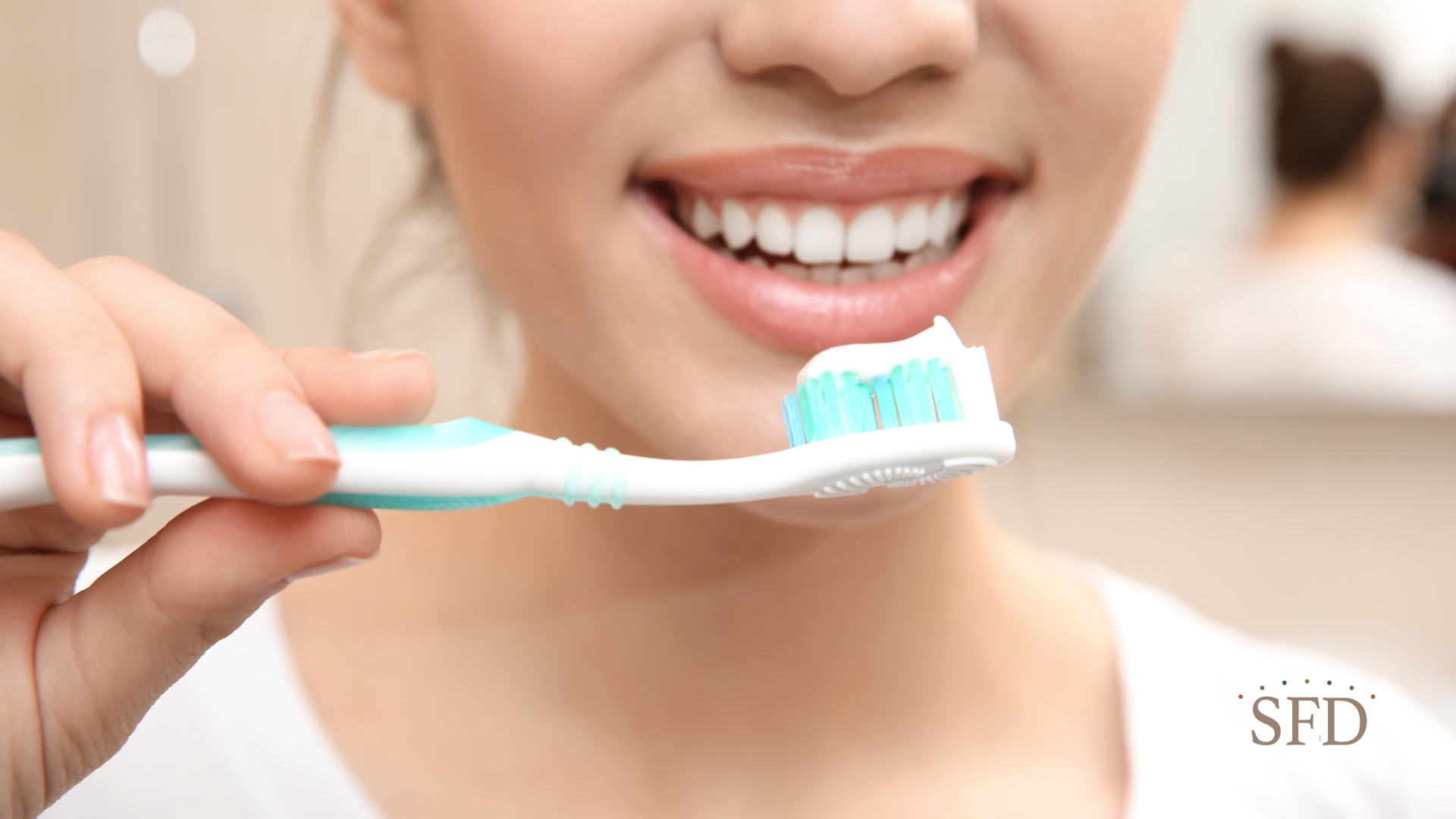 Woman smiling, holding toothbrush with toothpaste, ready to brush teeth in bathroom.