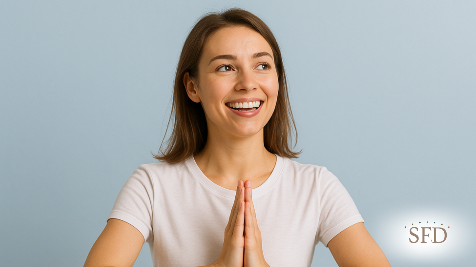 A woman is smiling with her hands folded in prayer.