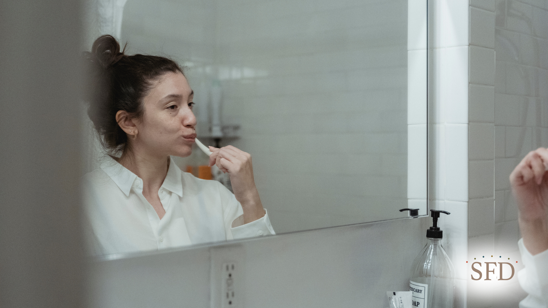 A woman is brushing her teeth in front of a bathroom mirror.