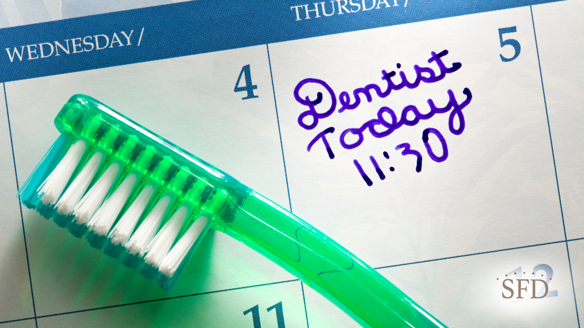 A green toothbrush is sitting on top of a calendar that says dentist today