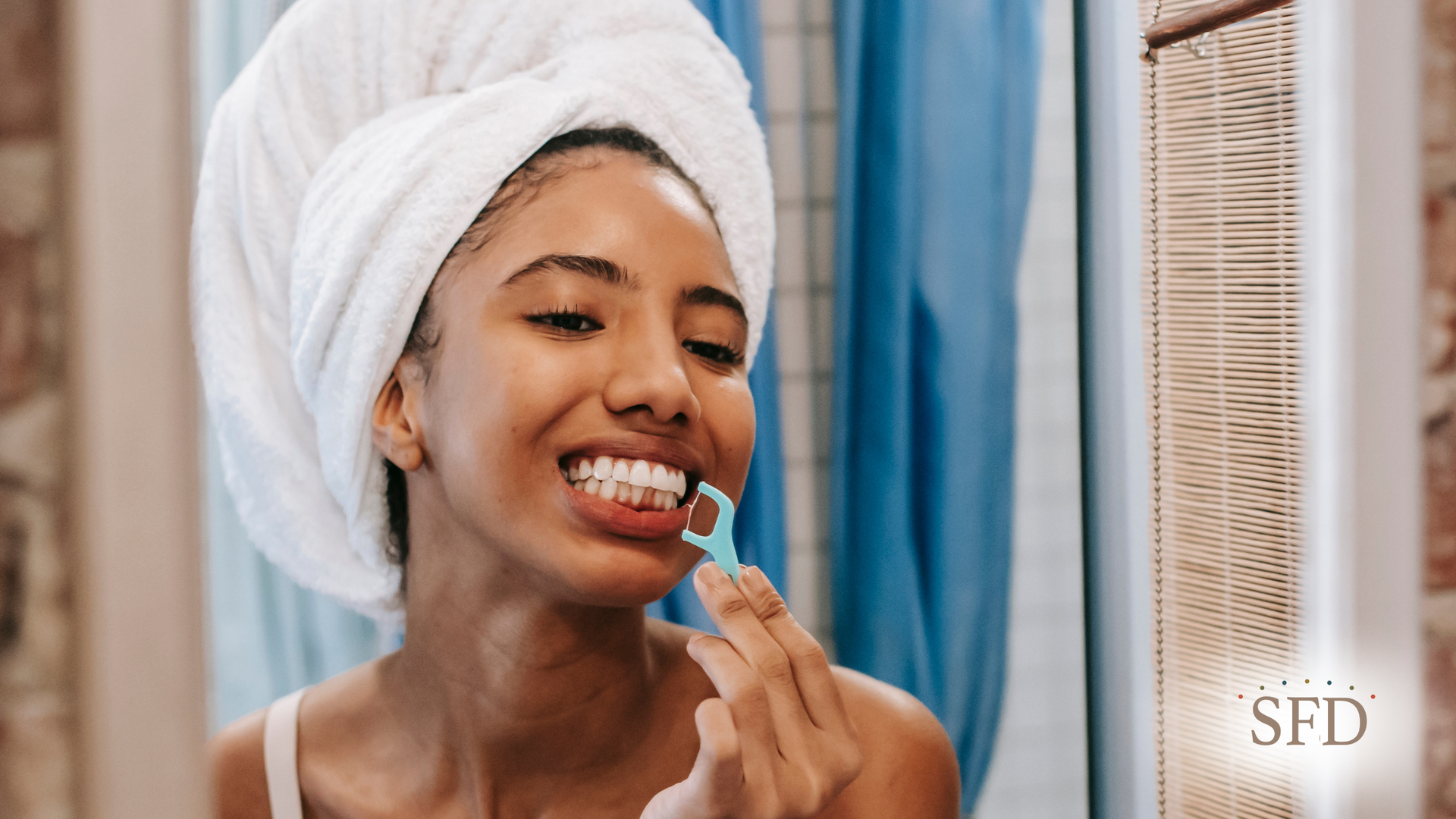A woman with a towel wrapped around her head is brushing her teeth in front of a mirror.
