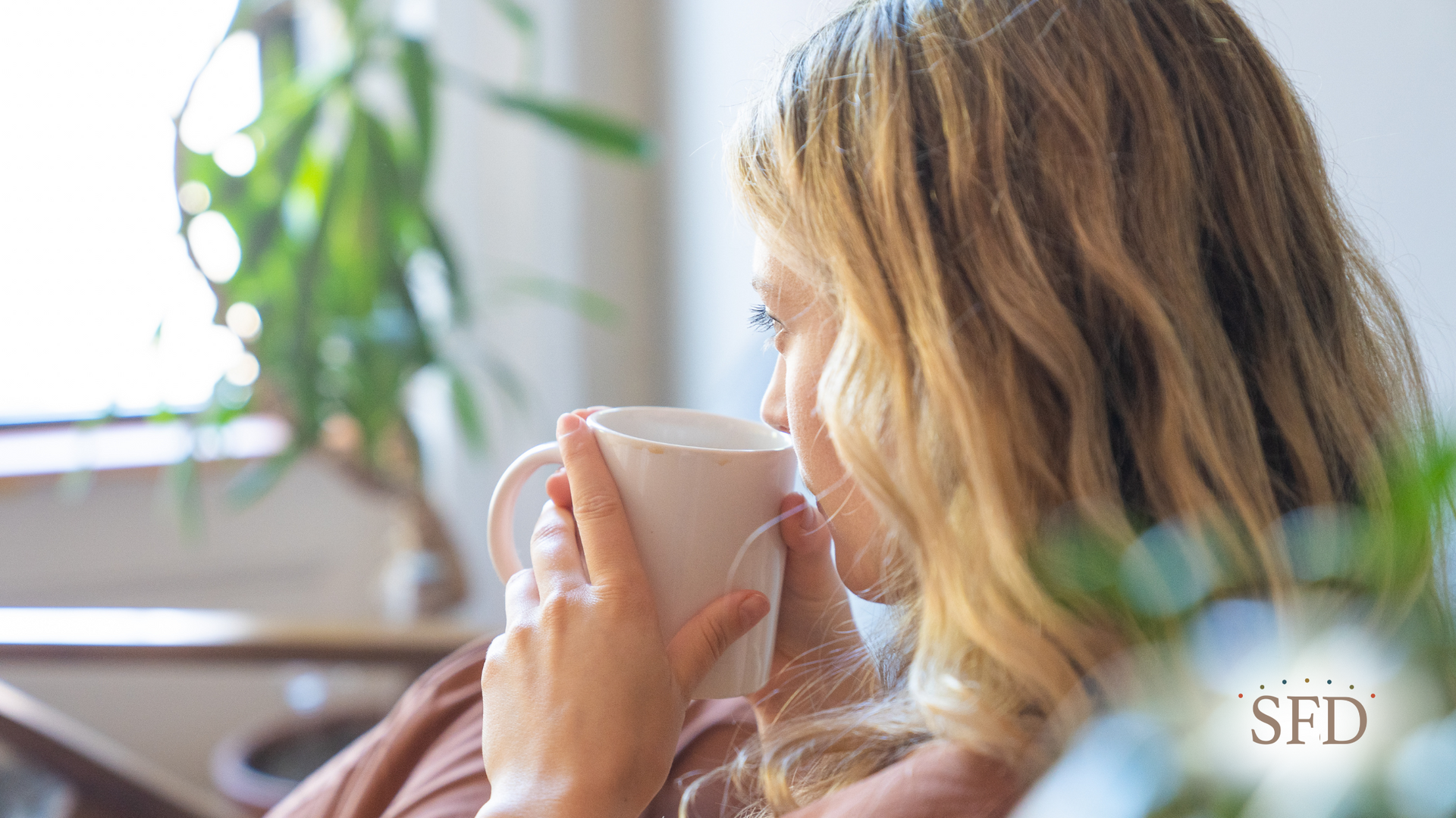 A woman is drinking a cup of coffee while sitting in a chair.