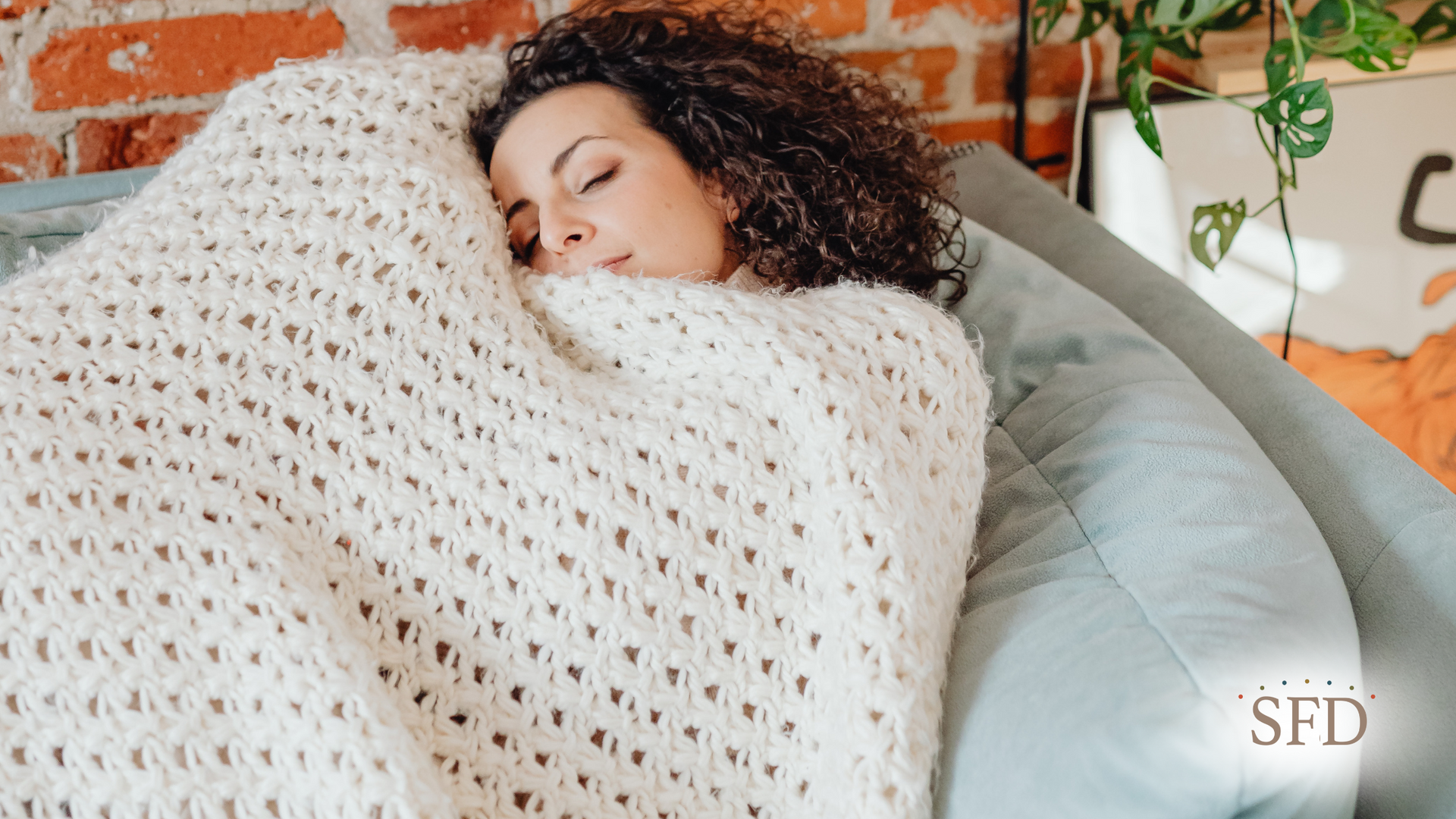 A woman is sleeping on a bean bag chair wrapped in a blanket.