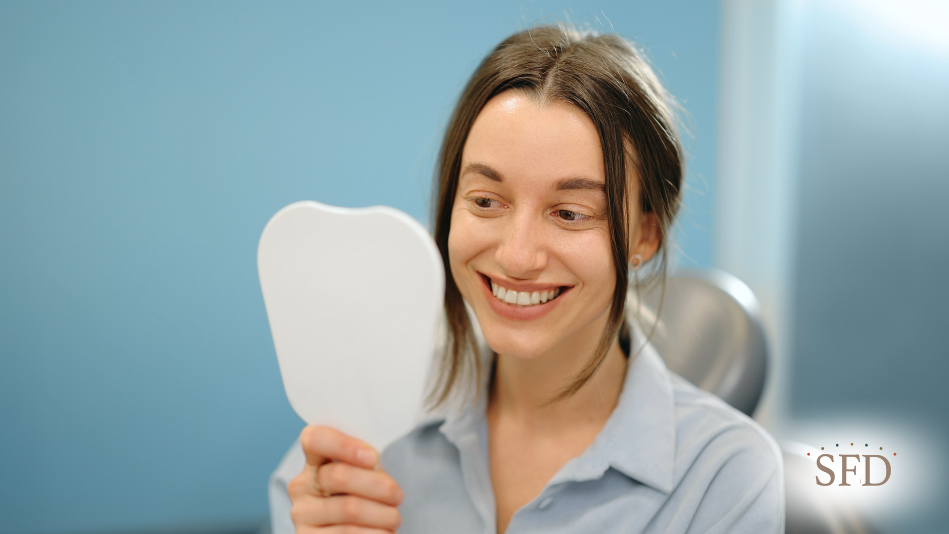A woman is smiling while looking at her teeth in a mirror.
