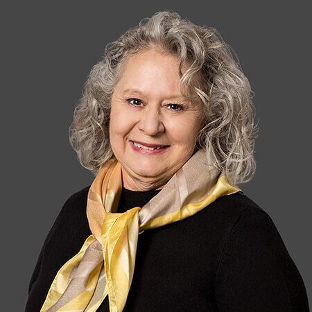 A woman with gray hair is wearing a black sweater and a yellow scarf.