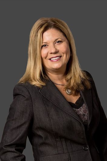 A woman in a suit and necklace is smiling for the camera.