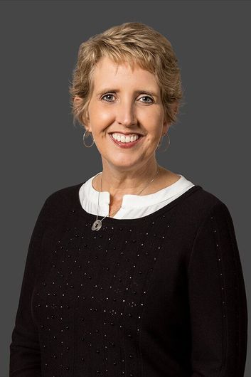 A woman in a black sweater and white shirt is smiling for the camera.