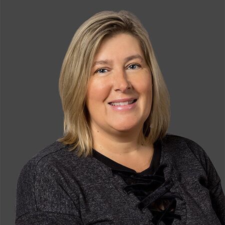 A woman in a gray sweater is smiling for the camera.