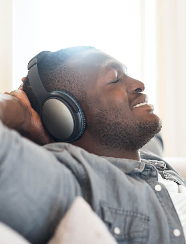 A man is sitting on a couch wearing headphones and listening to music.