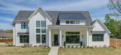 A large white house with a gray roof and black windows is for sale.