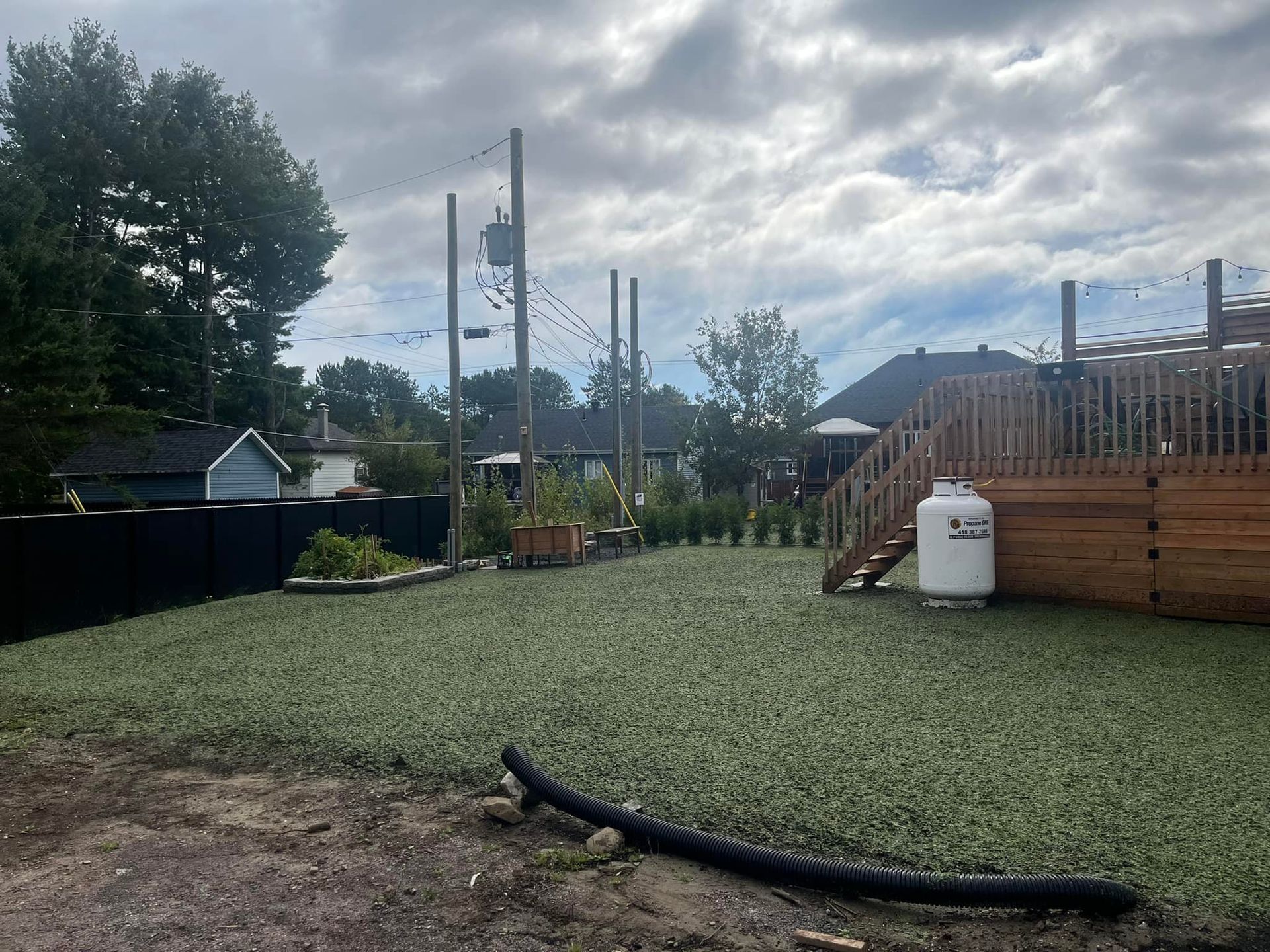 Une cour arrière avec une terrasse et un tuyau au milieu.