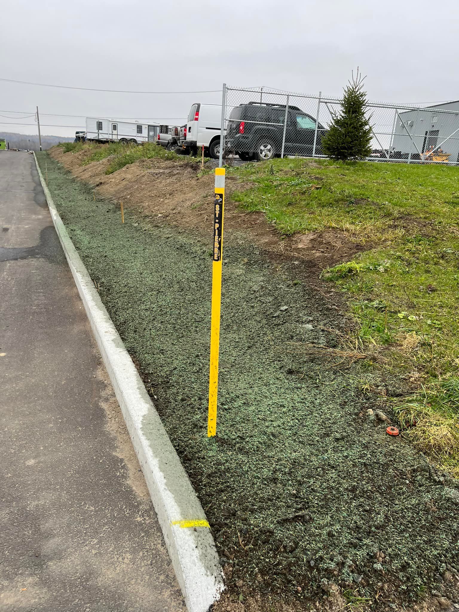 Un poteau jaune est posé sur le bord d'une route à côté d'une colline herbeuse.