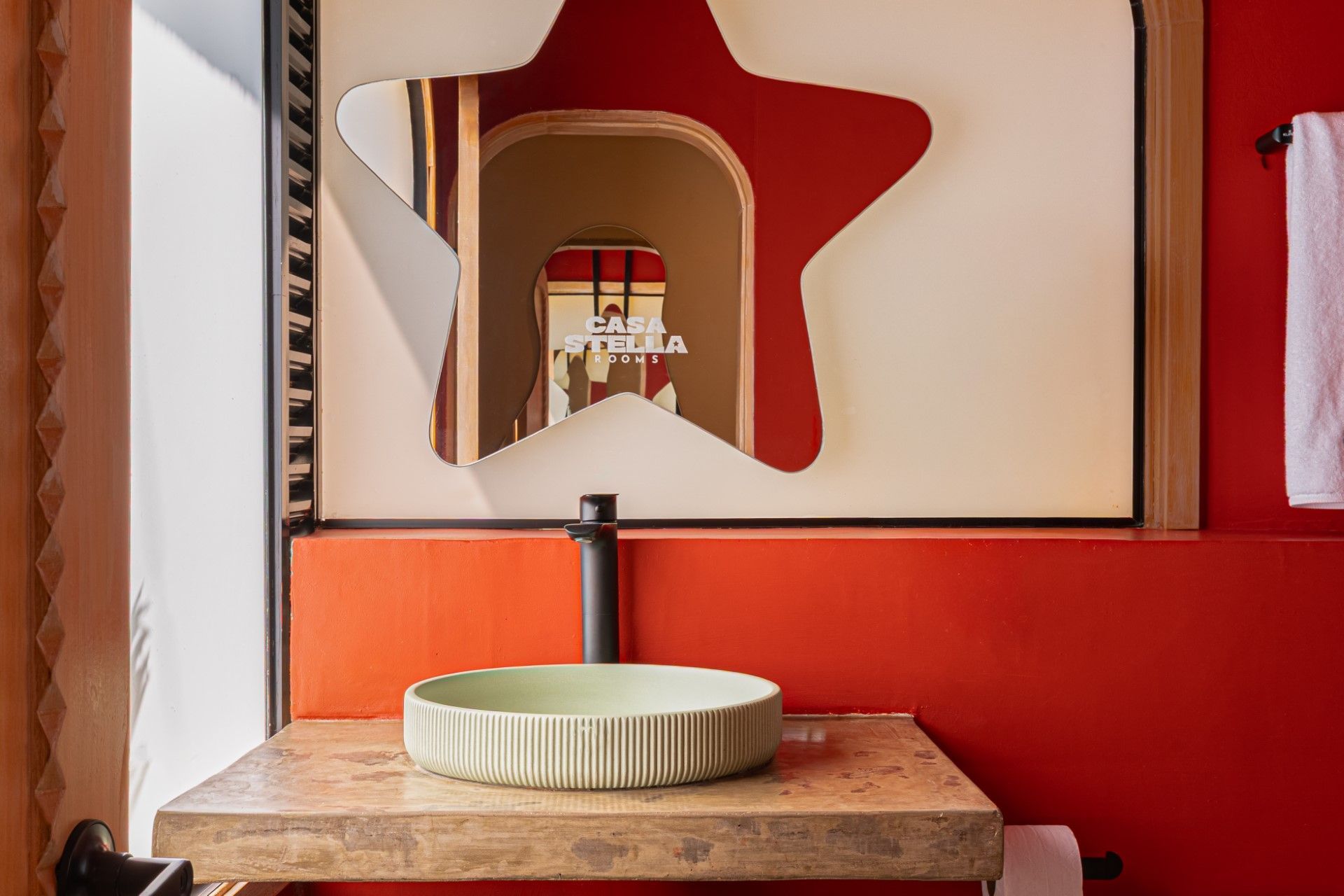 Baño con espejo en forma de estrella, pared roja, lavabo verde claro y encimera de madera.