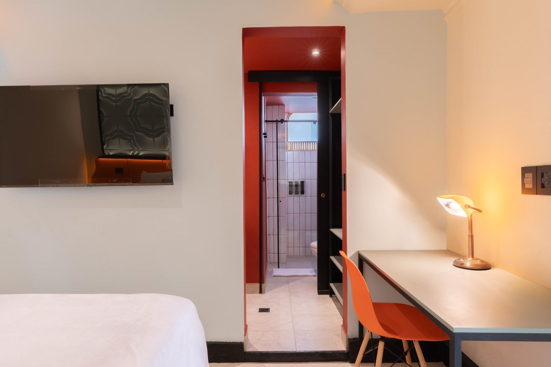 Interior de dormitorio con escritorio, silla naranja y puerta que conduce a un baño.