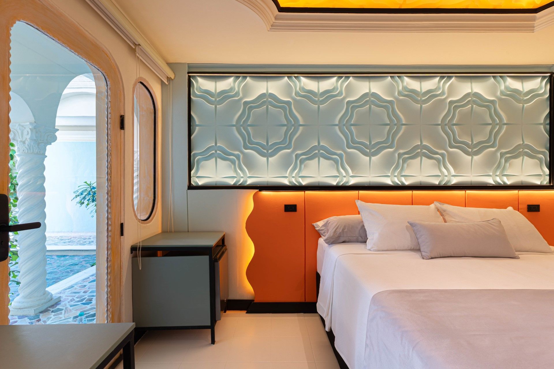 Dormitorio con cama, cabecero naranja, panel de pared decorativo y puerta arqueada.