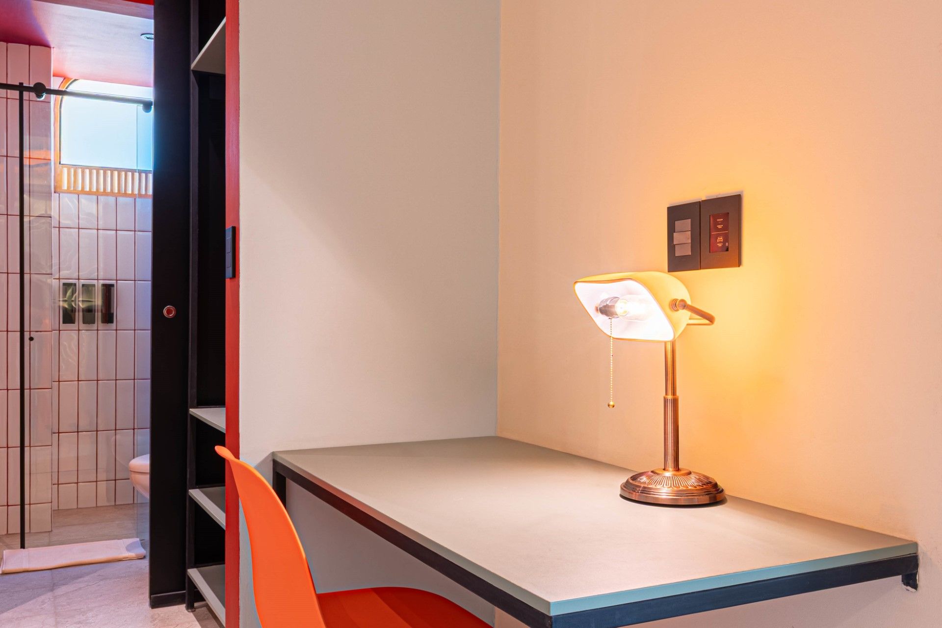 Escritorio con lámpara y silla naranja, junto a una puerta abierta. La pared es naranja claro.